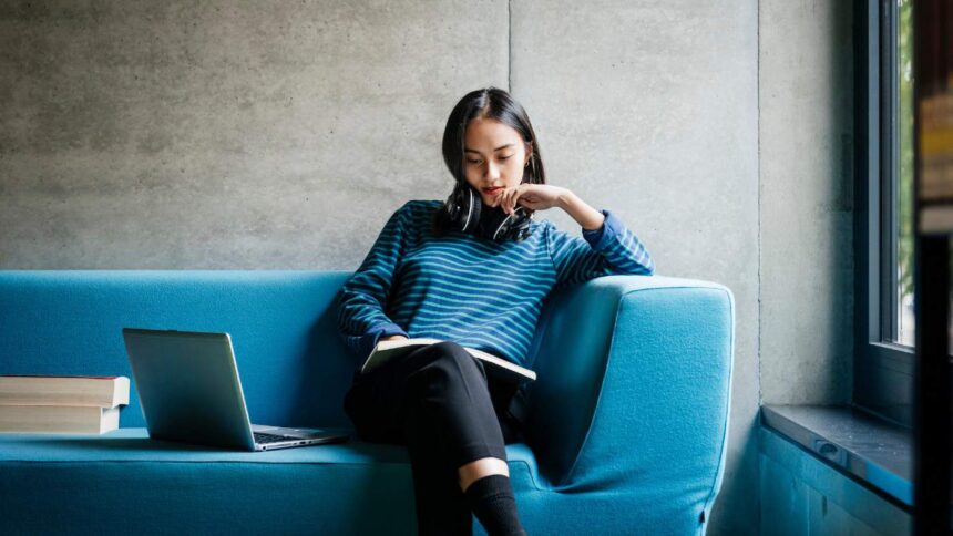 A young woman sitting on a couch looking at a book in a quiet library space.