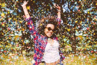 Young mixed-race woman jumping for joy in a park with confetti falling around her