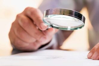 Person holding magnifying glass over important document, reading the small print