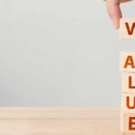 Hand of person putting wood cube block with word VALUE on wooden table