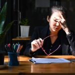 Young Asian woman with head in hands at her desk