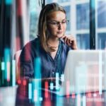 Young woman working at modern office. Technical price graph and indicator, red and green candlestick chart and stock trading computer screen background.