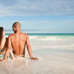 Young mixed-race couple sat on the beach looking out over the sea