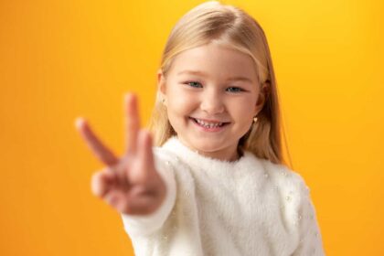 Young Caucasian girl showing and pointing up with fingers number three against yellow background