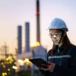 Petrochemical engineer working at night with digital tablet inside oil and gas refinery plant